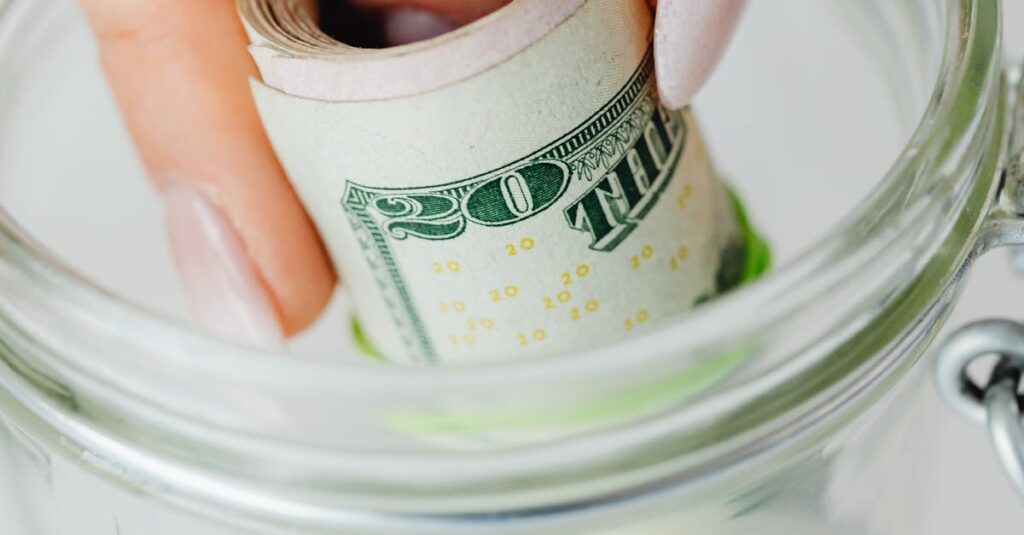 Hand placing rolled US dollars into a glass jar, representing savings and financial planning.
